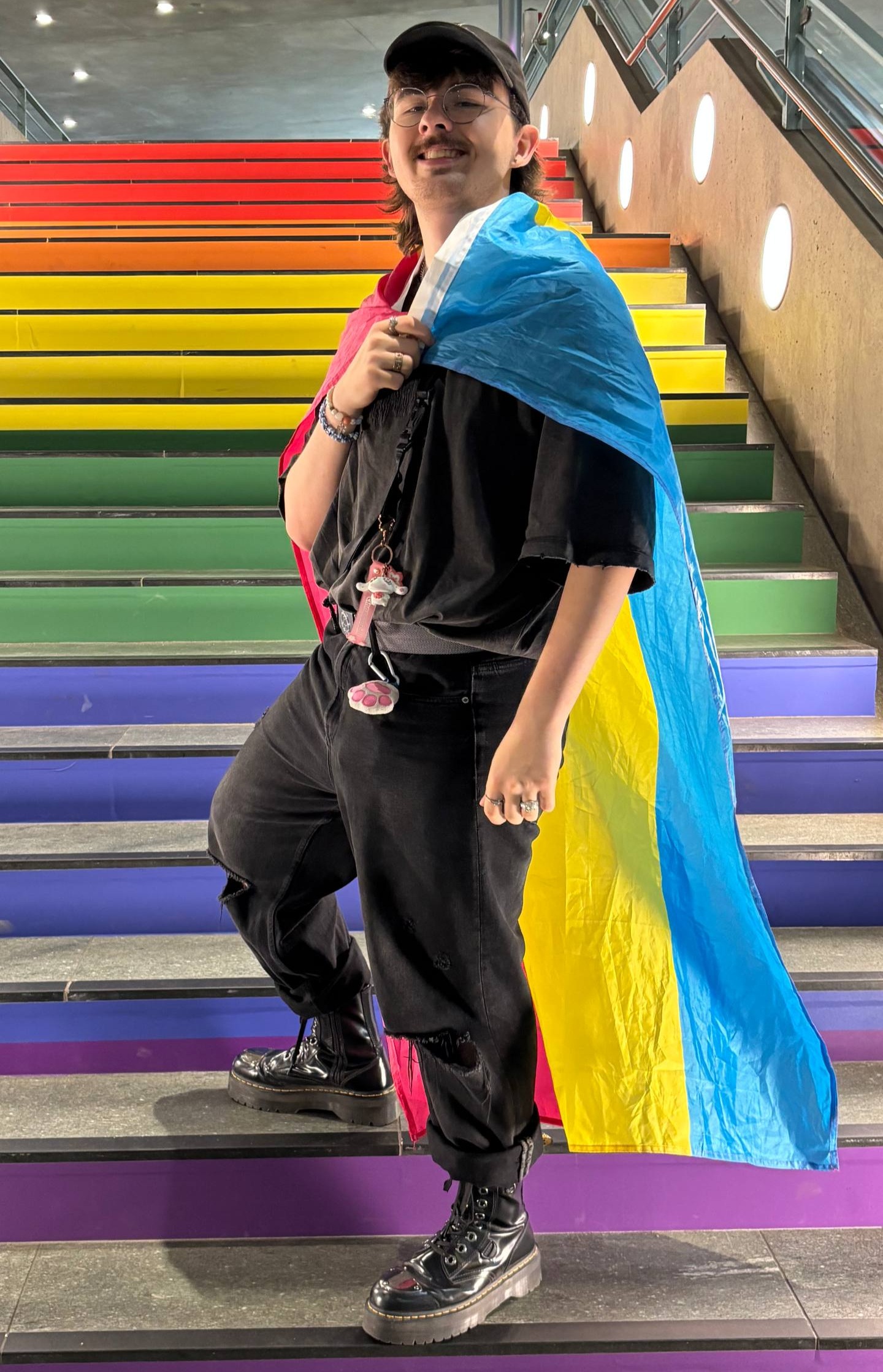 Photo of Olaf Börner from July 2025; smiling, waving a pansexual pride flag infront of the pride stairs at U-bahnhof Rotes Rathaus Berlin